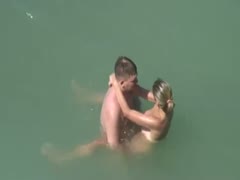 On a nudist beach, a horny couple is having sex in the sea.